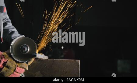 Forge workshop. Smithy manual production. Close up details of sparks, industrial worker using angle grinder and cutting steel. Stock Photo