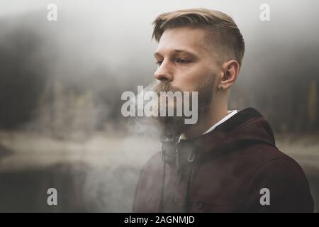 Handsome bearded man smoking cigarette Blows out steam through the nostrils Stock Photo