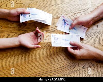Hands of a man giving fifthy thousand pesos bills to a Young that is asking for more money over a table Stock Photo