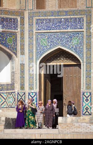 Women in traditional clothing in front of the entrance portal of the Mir-Arab-Madrasa, Old Town, Bukhara, Bukhara Province, Uzbekistan Stock Photo