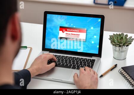 Virus detected warning message on computer screen, Cyber attack concept. Man working on a laptop, office business wood desk background. Stock Photo