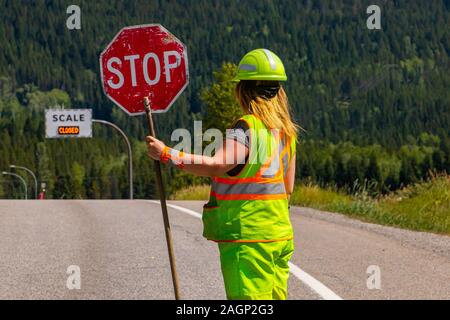 A close up and rear view of a female road construction worker holding a stop stick wearing high visibility safety clothes, roadworks traffic control Stock Photo