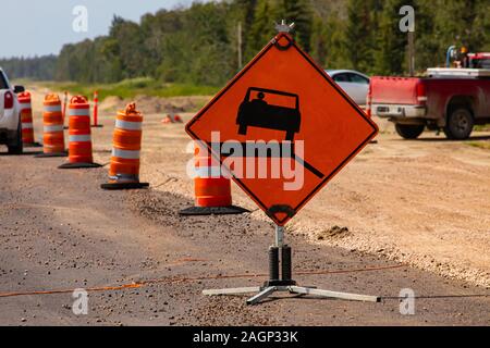 A steep verge warning sign, bright orange danger road sign, is seen close up during roadworks on a main road, with cones and copy space in background Stock Photo