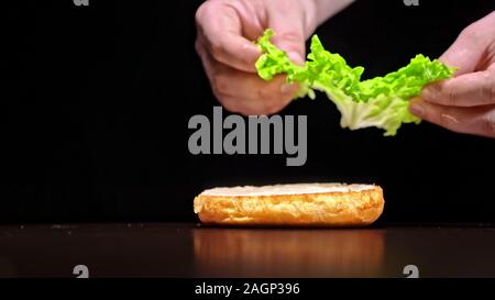Craft burger is cooking on black background. Consist: sauce, lettuce, tomato, red onion, pickle, cheese, bacon, air bun and marbled meat beef. Stock Photo