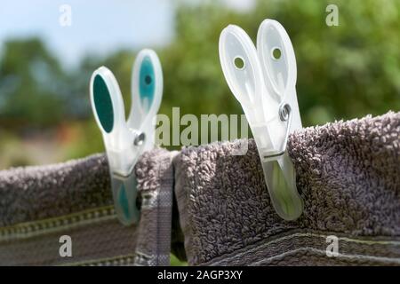 Close-up of two dark towels drying on a clothesline with two large green and yellow clothespins against a blue and green background Stock Photo