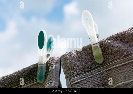 Close-up of two dark towels drying on a clothes line with two large green and yellow clothespins against a blue cloudy sky Stock Photo