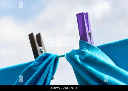 Close-up of two blue shirts drying on a clothes line with a purple and black clothespin against a cloudy sky Stock Photo