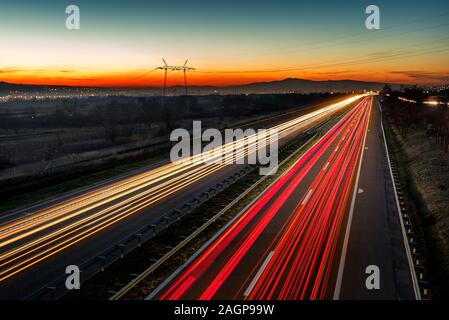 Cars light trails on a straight highway at sunset. Night traffic trails, Motion blur, Night city road with traffic headlight motion. Stock Photo