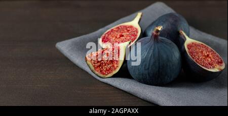 Fresh figs on dark background with copy space. Purple ripe sliced and whole figs on a grey napkin. Side view. Figs on brown wooden background. Stock Photo
