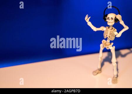 A skeleton enjoys listening to his / her music on their headphones. Taken on a blue background.