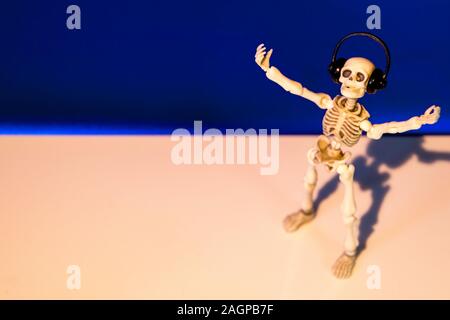 A skeleton enjoys listening to his / her music on their headphones. Taken on a blue background.