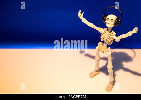 A skeleton enjoys listening to his / her music on their headphones. Taken on a blue background.