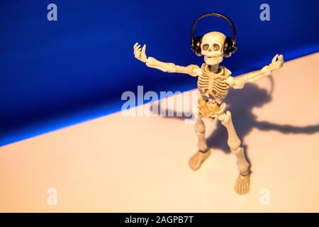 A skeleton enjoys listening to his / her music on their headphones. Taken on a blue background.