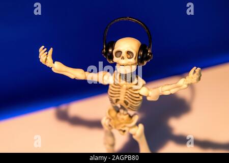 A skeleton enjoys listening to his / her music on their headphones. Taken on a blue background.