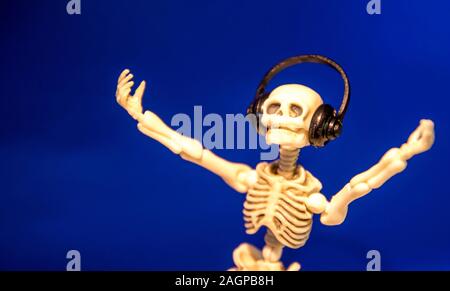 A skeleton enjoys listening to his / her music on their headphones. Taken on a blue background.