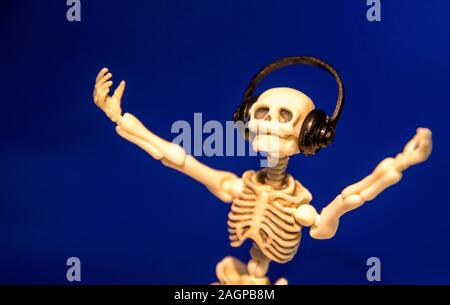 A skeleton enjoys listening to his / her music on their headphones. Taken on a blue background.