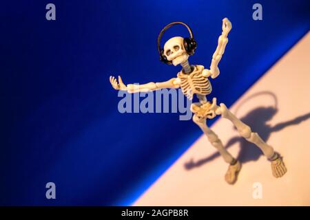 A skeleton enjoys listening to his / her music on their headphones. Taken on a blue background.