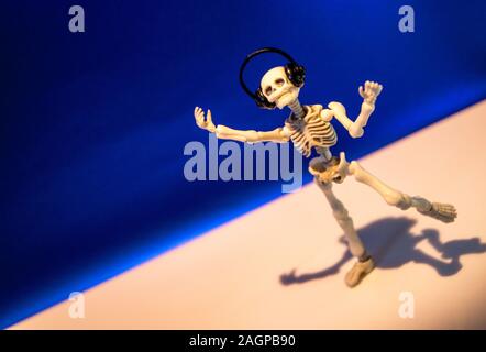 A skeleton enjoys listening to his / her music on their headphones. Taken on a blue background.