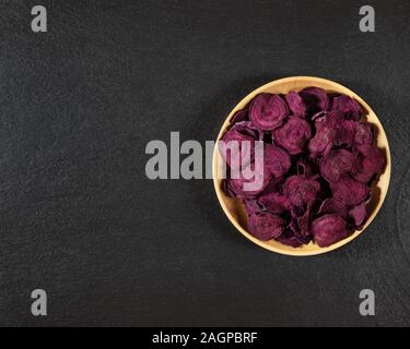 Dried beet chips in a wooden bowl on a black stone background. Organic natural food. Top view, flat lay. Copy space. Stock Photo