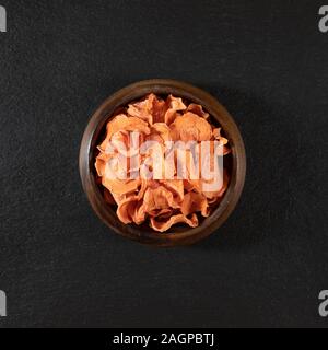 Dried carrot chips in a wooden bowl on a black stone background. Organic natural food. Top view, flat lay. Stock Photo