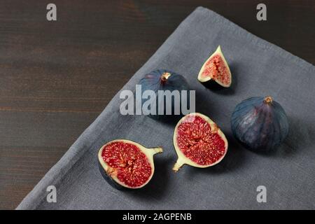 Fresh figs on dark background. Copy space. Purple ripe sliced and whole figs on a grey napkin. Side view. Figs on brown wooden background. Stock Photo