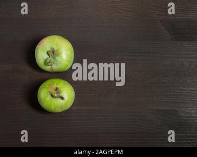 Trendy ugly food concept. Two green apples on a dark brown wooden background. Copy space. Fruit with a strange shape. Stock Photo