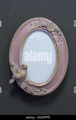 Empty pink-gold vintage oval frame in Victorian style on a gray wall, background or concept Stock Photo