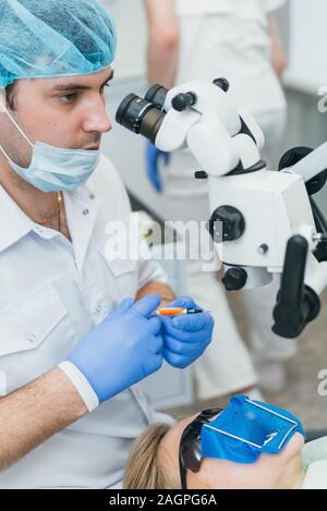 Doctor used microscope. Dentist is treating patient in modern dental office. Operation is carried out using cofferdam. Client is inserted and restored Stock Photo