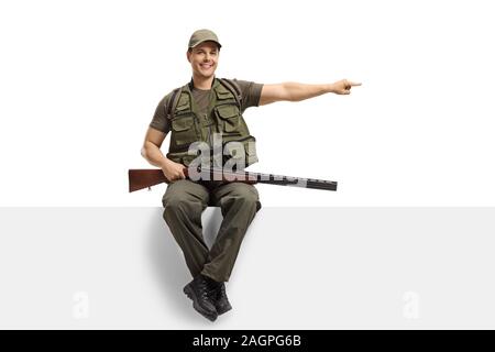 Male hunter with equipment sitting on a panel and pointing to the side isolated on white background Stock Photo