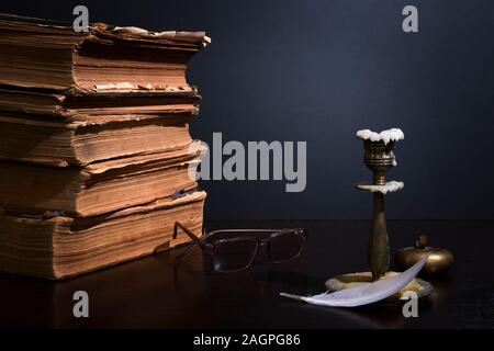 Stack of ancient books with yellowed shabby pages, glasses, candlestick with blown wax and little bronze pocket ashtray Stock Photo