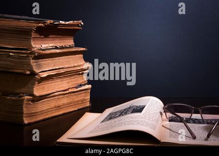 Stack of ancient books with yellowed shabby pages and open book with glasses on it