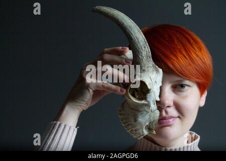 Portrait of a middle-aged redhead woman holding half a goat skull in front of her face, duplicity concept Stock Photo