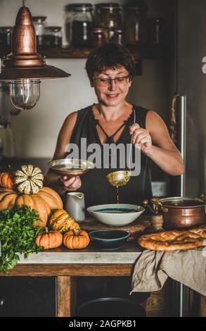 Elderly woman serving Autumn seasonal pumpkin cream soup Stock Photo