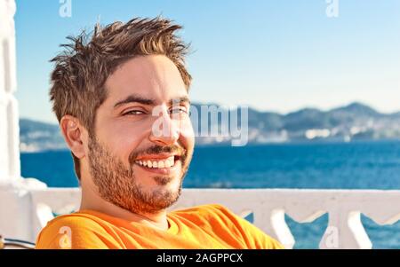 Happy young caucasian man with an orange t-shirt smiling on summer vacation beside the sea in Spain Stock Photo