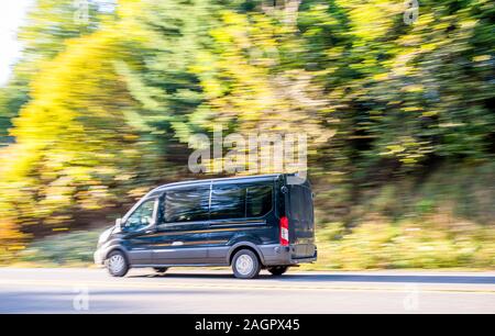 Black comfortable compact commercial cargo mini van for local freight and deliveries and small business needs running on autumn road with green and ye Stock Photo