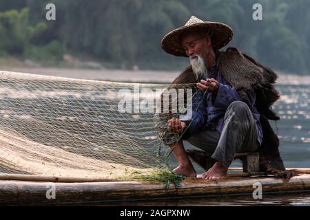 Xingping, China - November 5, 2019: Portrait of a cormorant fisherman at sunset using a traditional fishing method to catch the fish in the river Stock Photo
