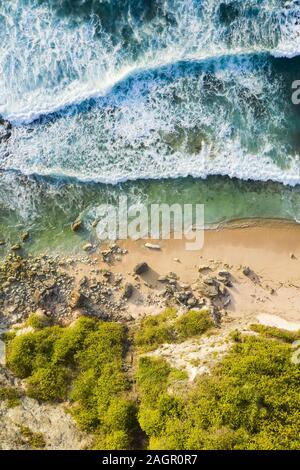 View from above, stunning aerial view of a rocky shore with a beautiful beach bathed by a rough sea during sunset, Nyang Nyang Beach, Bali, Indonesia. Stock Photo