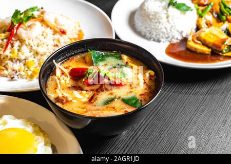 Selective focus of Thai dishes on the table. Tom yum soup, Olive fried rice, Mixed Vegetables fried rice in the background blurred. Stock Photo