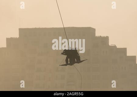 Military team in conflict rescuing people by helicopter. flying through the air on a rope attached to chopper in the smoke and haze in the MIddle East Stock Photo