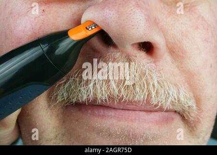 Elderly old man cuts hairs in his nose  with an electric hair clipper. Studio macro natural colors simplistic image Stock Photo