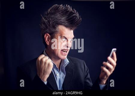 Handsome man with mohawk wearing suit using mobile phone in front of black background. Stock Photo
