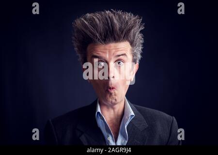 Man with funny haircut wearing suit showing emotions in front of black background. Stock Photo