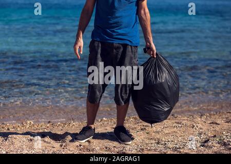 Man volunteer with black bag collect garbage on the beach. Environmental pollution concept Stock Photo