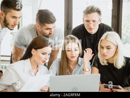Group of six students with drawings schemes and laptop is working with project Stock Photo