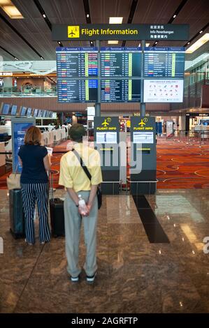 06.12.2019, Singapore, Republic of Singapore, Asia - Travelers in front of a flight information display at Changi Airport Terminal 1. Stock Photo