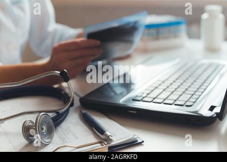 Female doctor diagnostician at his workplace in the hospital. Works on laptop with x-ray and medical tests. Stock Photo