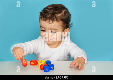 Jewish boy playing with colorful wood dreidel. Kid celebrating Hanukkah Israel holiday. Stock Photo