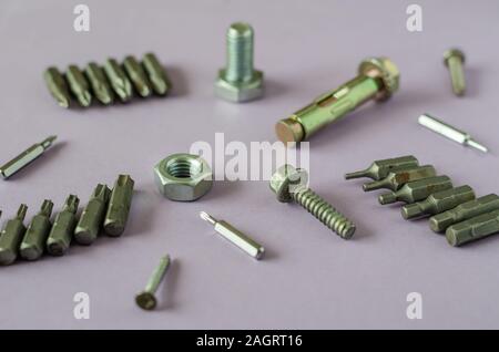 Used bits and new bots. Side view of Screwdriver Bit Sets, Bolts, Nuts, Screws and Anchor Bolt on a light pink background. Selective focus. Close-up. Stock Photo