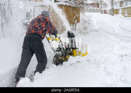 man operating snow blower to remove snow on driveway. Man using a snowblower. A man cleans snow from sidewalks with snowblower. Stock Photo