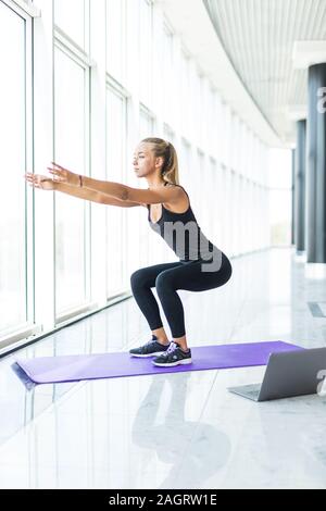 Girl makes yoga exercise online with laptop at gym Stock Photo